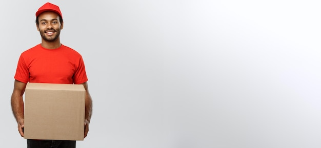 Delivery Concept Portrait of Happy African American delivery man in red cloth holding a box package Isolated on Grey studio Background Copy Space