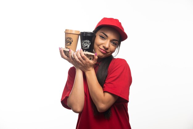 Delivery employee woman in red cap hugging two cups of coffee