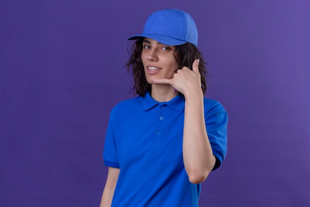 Free photo delivery girl in blue uniform and cap making call me gesture smiling friendly on isolated purple