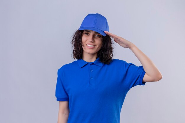 Delivery girl in blue uniform and cap saluting  smiling friendly over isolated white space