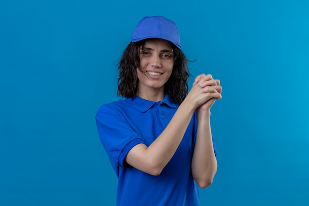 Free Photo delivery girl in blue uniform and cap standing with a gesture of teamwork smiling friendly on isolated blue