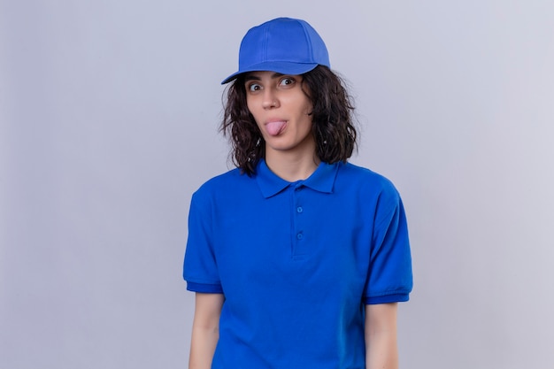 Delivery girl in blue uniform and cap sticking tongue out happy with funny expression standing on isolated white