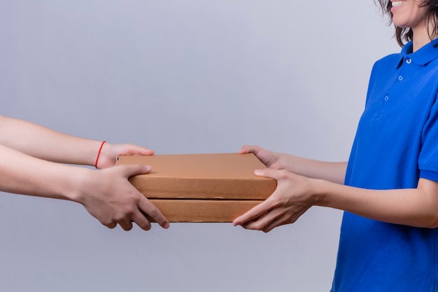 Delivery girl in blue uniform giving pizza boxes to u customer over isolated white space