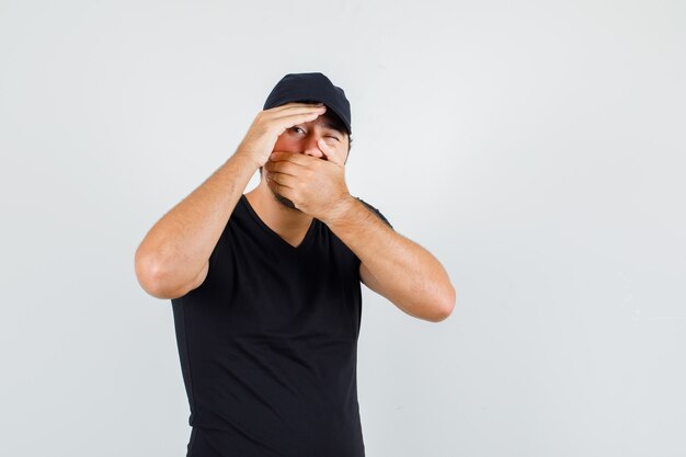 Delivery man in black t-shirt, cap covering mouth and winking eye