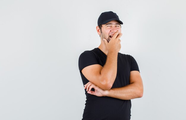 Delivery man in black t-shirt, cap laughing with hand on mouth