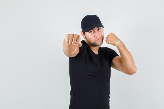 Delivery man in black t-shirt, cap standing in boxer pose and looking confident