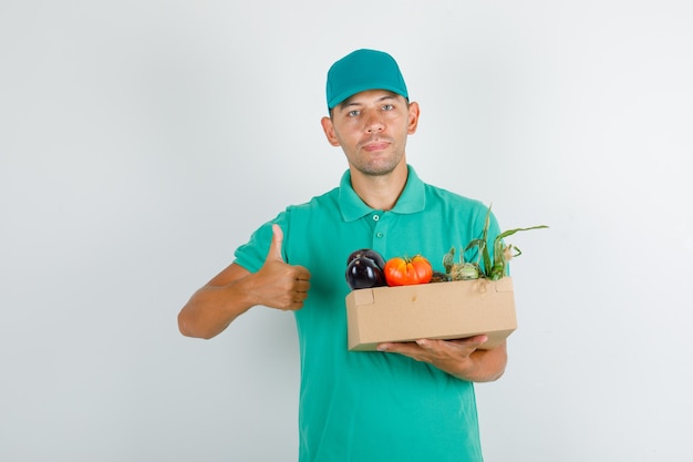 Free photo delivery man in green t-shirt and cap holding vegetable box with thumb up