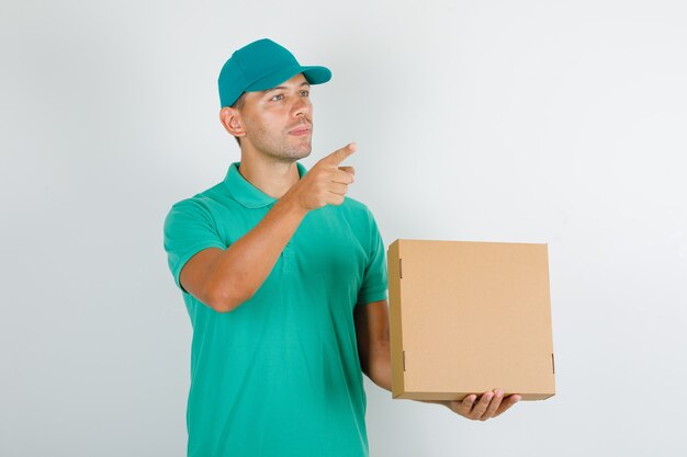 Delivery man in green t-shirt and cap showing something with cardboard box