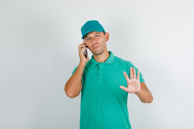 Delivery man in green t-shirt with cap talking on phone with stop sign