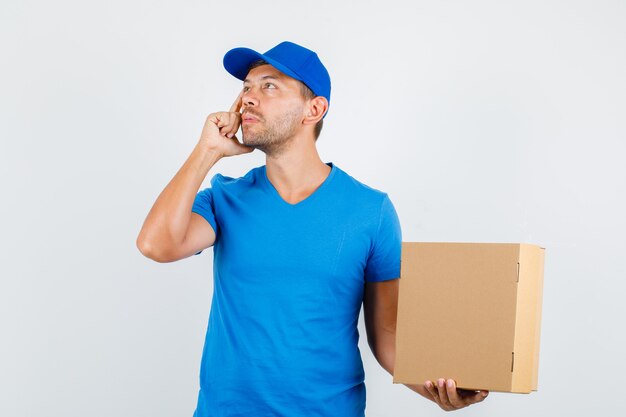 Delivery man holding cardboard box while looking up in blue t-shirt