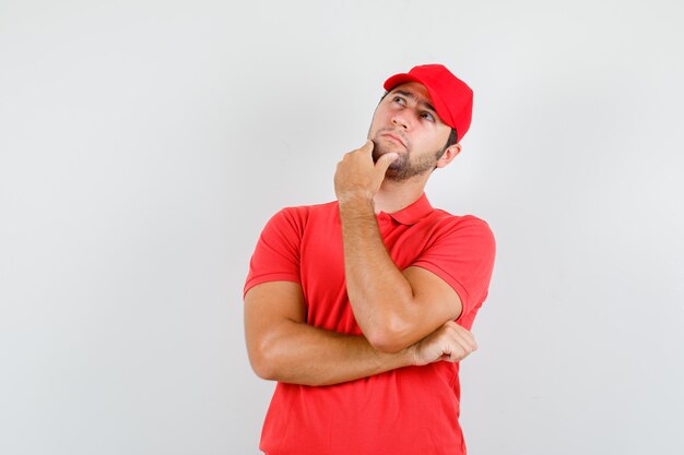 Delivery man looking up while touching chin in red t-shirt