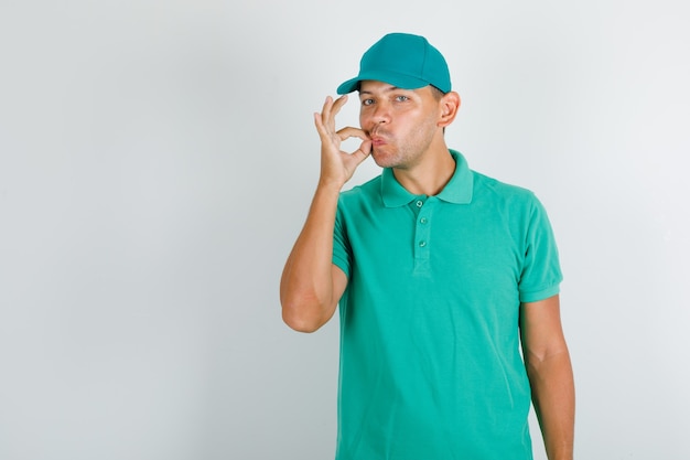 Delivery man making delicious gesture in green t-shirt with cap