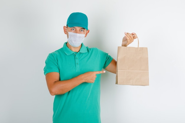 Free photo delivery man pointing paper bag with finger in green t-shirt with cap