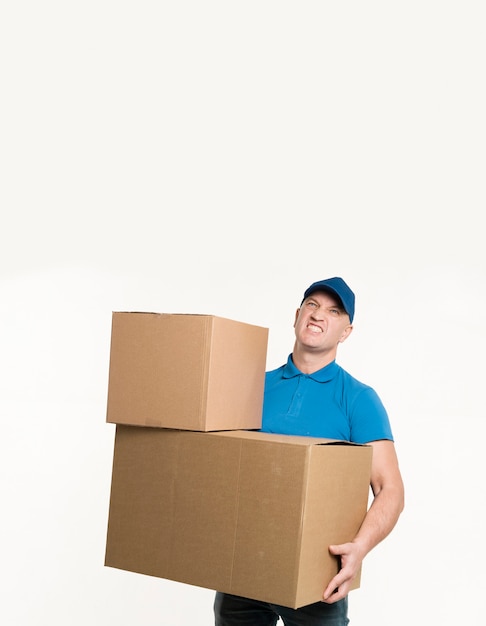 Free Photo delivery man posing while holding heavy cardboard boxes