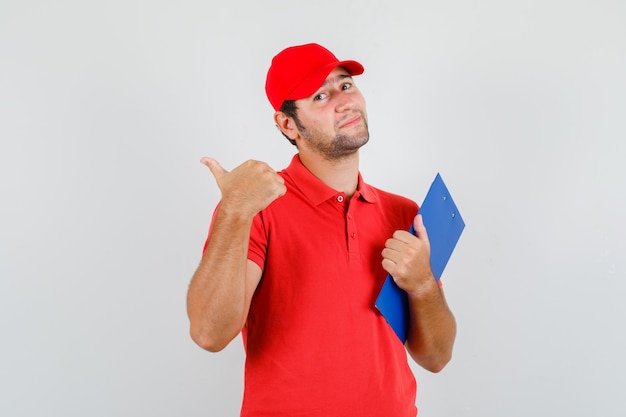 Delivery man in red t-shirt, cap holding clipboard and showing thumb up