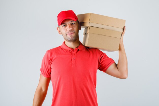 Delivery man in red uniform holding cardboard boxes on his shoulder