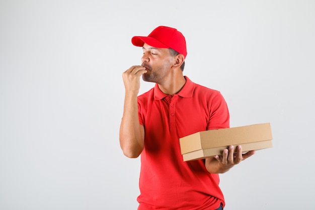 Delivery man in red uniform making tasty gesture while holding pizza box