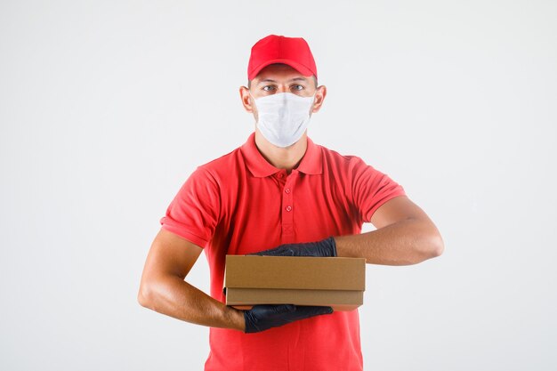 Delivery man in red uniform, medical mask, gloves holding cardboard box