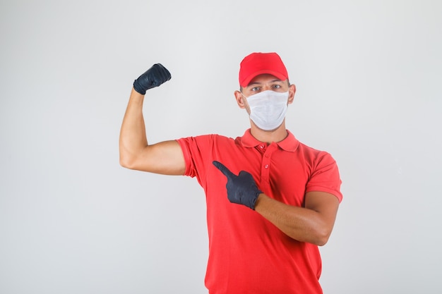 Delivery man in red uniform, medical mask, gloves showing biceps and looking powerful