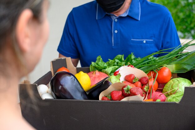 Delivery man wearing a face mask and holding a box with vegetables