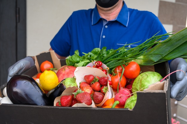 Delivery man wearing a face mask and holding a box with vegetables