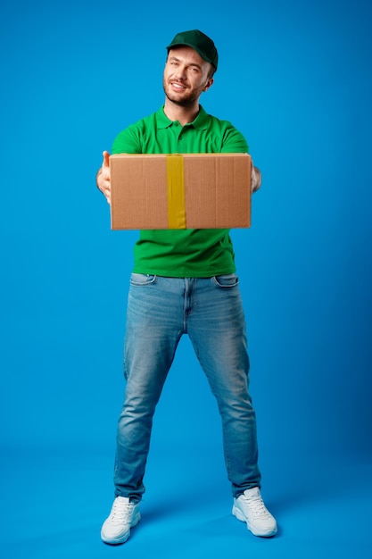 Delivery man with box in studio against blue background