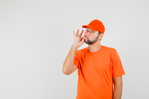 Delivery man zipping his mouth shut in orange t-shirt, cap , front view.