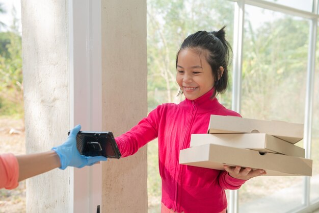 Delivery service in t-shirt, in protective mask and gloves giving food order, pizza boxes in front house, Young woman sign in digital mobile phone after receiving parcel from courier.COVID-19 outbreak