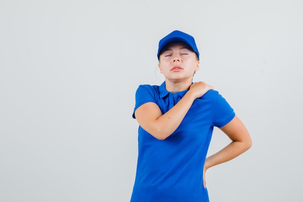 Delivery woman in blue t-shirt and cap suffering from shoulder pain and looking tired