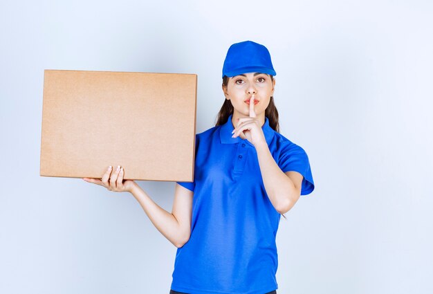 Delivery woman employee with craft paper box showing silent sign .