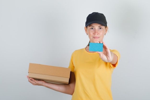 Delivery woman holding cardboard box and blue card in t-shirt and cap