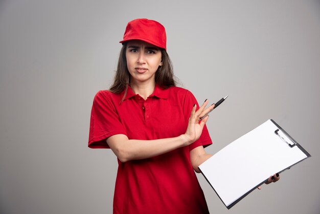 Delivery woman in red uniform staying away from clipboard. 