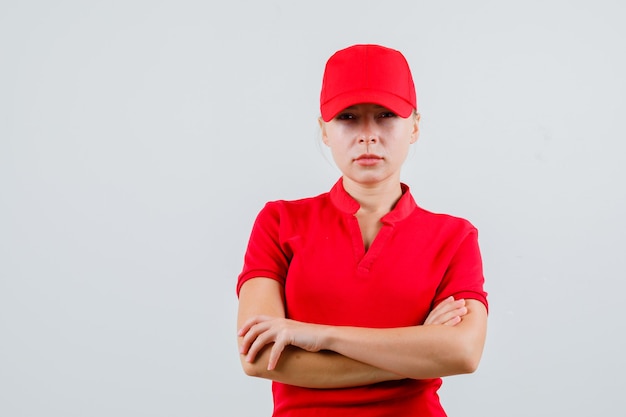 Free photo delivery woman standing with crossed arms in red t-shirt and cap and looking strict