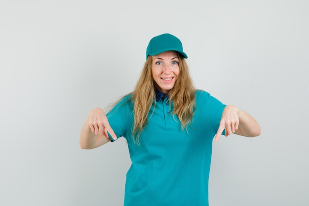 Delivery woman in t-shirt, cap pointing down and looking cheerful 