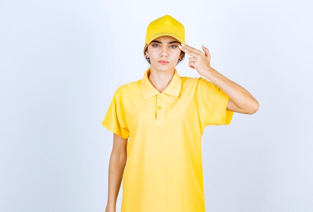 Delivery woman in yellow uniform holding two fingers near temple like a pistol.