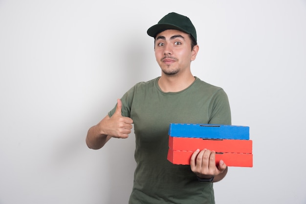 Free photo deliveryman pointing up and holding pizza boxes on white background.