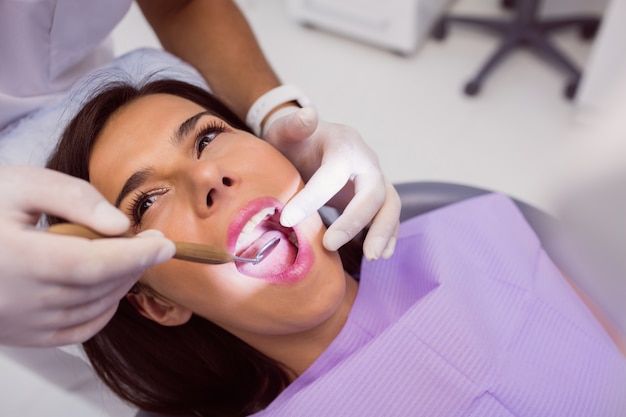 Dentist examining female patient teeth with a mouth mirror