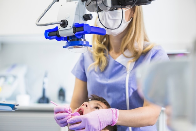 Free photo dentist examining patient's teeth through microscope in clinic