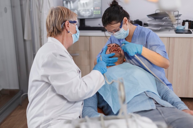 Dentist group of doctors with medical face masks using professional dental tools during stomatological surgery in dentistry hospital office room. Orthodontist doctor working at healthcare treatment