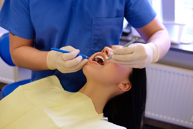 A dentist hands working on young woman patient with dental tools.