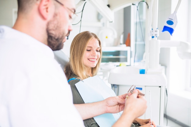 Dentist measuring plastic teeth model with vernier caliper near female patient