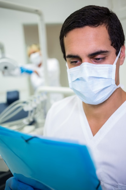 Dentist in surgical mask looking at a medical file