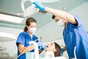 Free photo dentist treating patient with dental tool while male colleague adjusting light at clinic