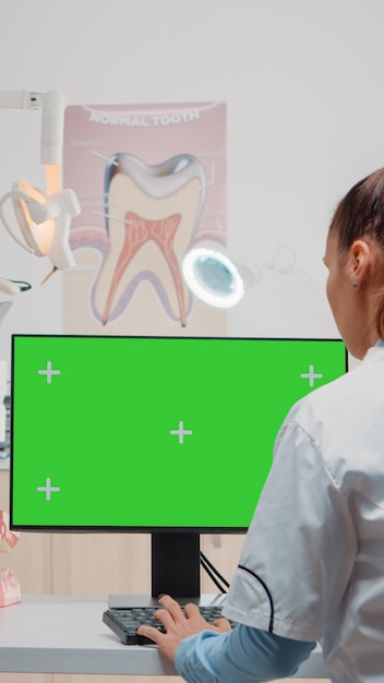 Free photo dentist using computer with horizontal green screen on display. specialist looking at monitor with chroma key and isolated template for oral care while asisstant using dental equipment