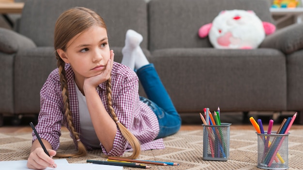 Free photo depressed girl lying on carpet drawing with colored pencil