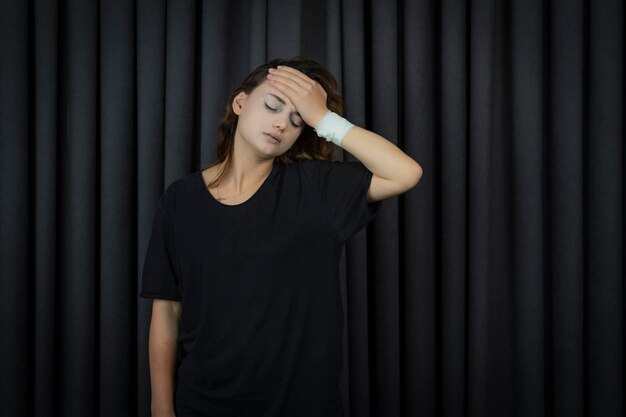 Depressed young girl stands on a black background and puts her hand to her forehead. High quality photo