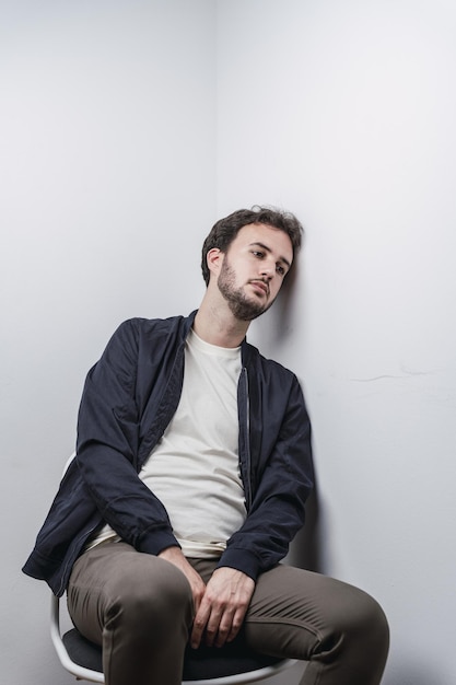 Depressed young Spanish male sitting on a chair leaning his head against a wall