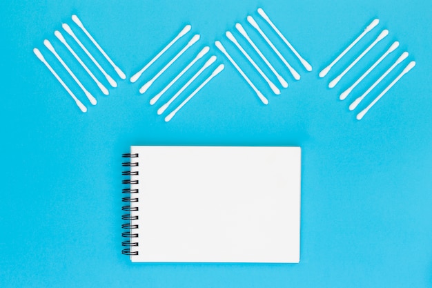 Design made with cotton swabs on blank spiral notepad on blue background