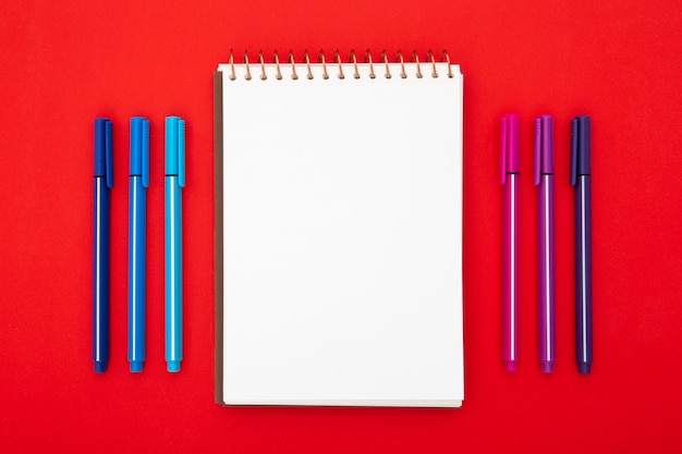 Desk arrangement with empty notepad on red background