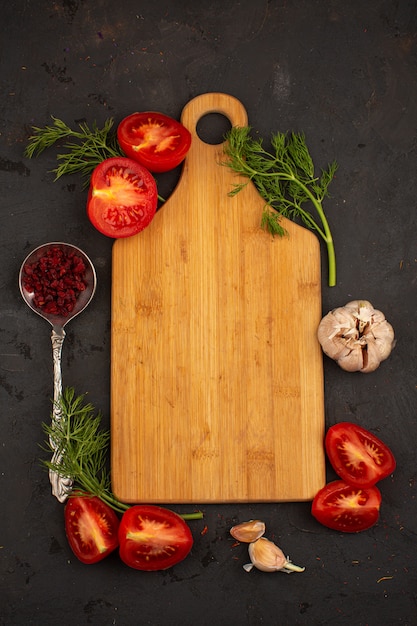 Desk vegetables sliced ripe fresh tomatoes and greens with garlic on a dark floor